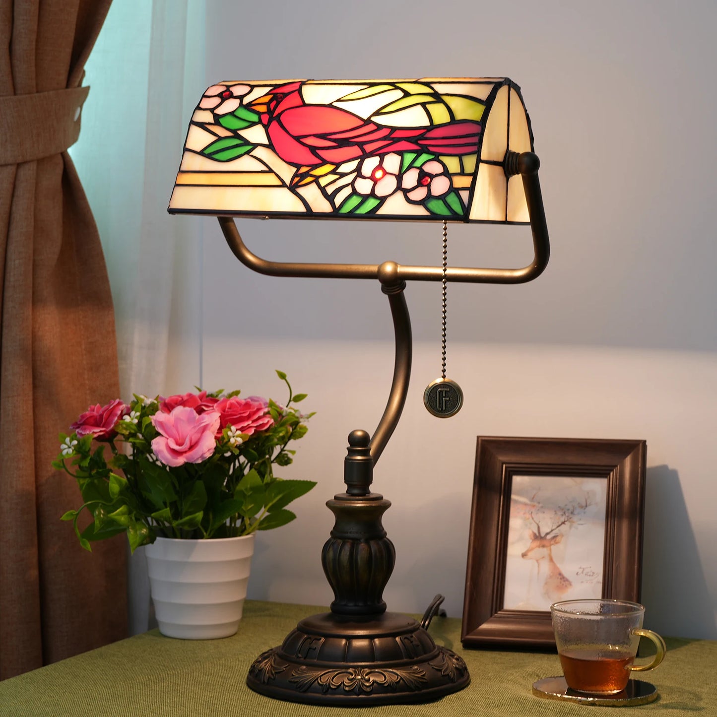 Decorative table lamp with stained glass design on a table with flowers and a cup.